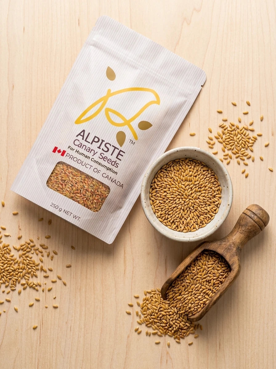 A stand-up pouch of Alpiste Canary Seeds for human consumption, styled on a light wood background with a small bowl, wooden scoop, and scattered seeds.